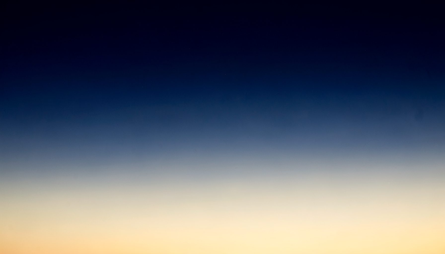Deep navy blue night sky fading into a warm cream horizon, with soft atmospheric haze and a calm, expansive mood